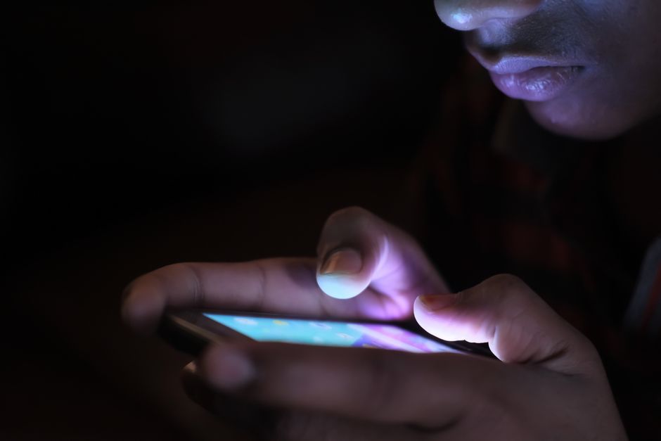 Close-up of a person holding and using an illuminated smartphone in a dark setting.
