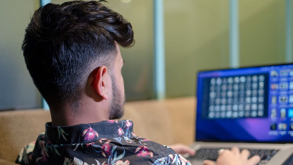 Man with short hair using a laptop indoors, viewed from behind. Floral shirt visible.