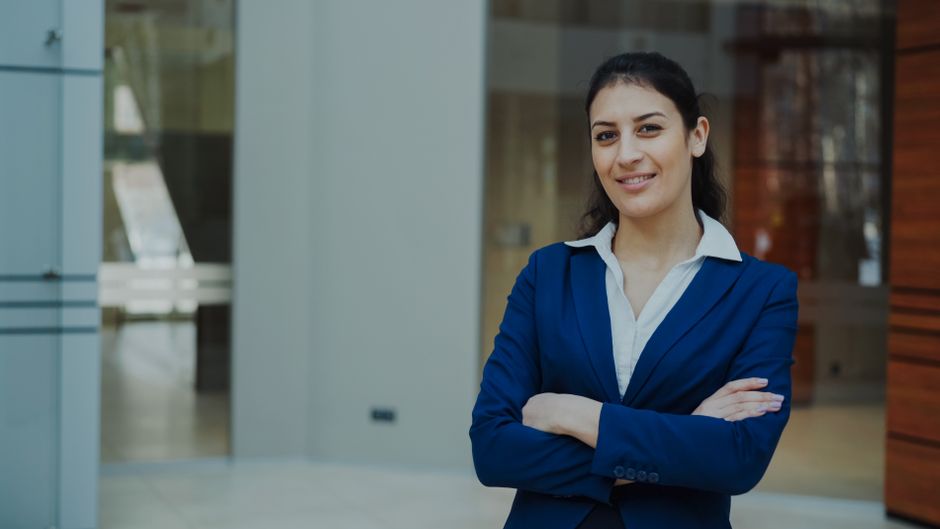 Professional woman in a blue suit smiling confidently in an office setting.