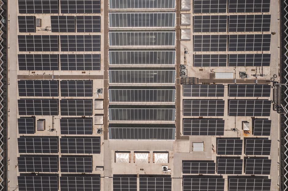 A high-angle drone shot capturing a grid of solar panels on a large industrial rooftop, showcasing renewable energy.