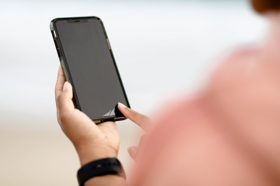 A hand interacting with a smartphone touchscreen outdoors. Modern technology concept.