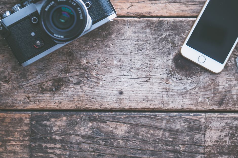 A flat lay of a vintage camera and smartphone on a rustic wooden table, ideal for tech and photography themes.