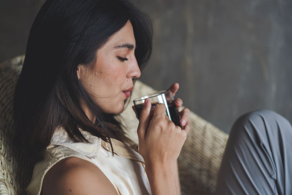 Woman savoring a cup of coffee while relaxing in a cozy chair indoors.