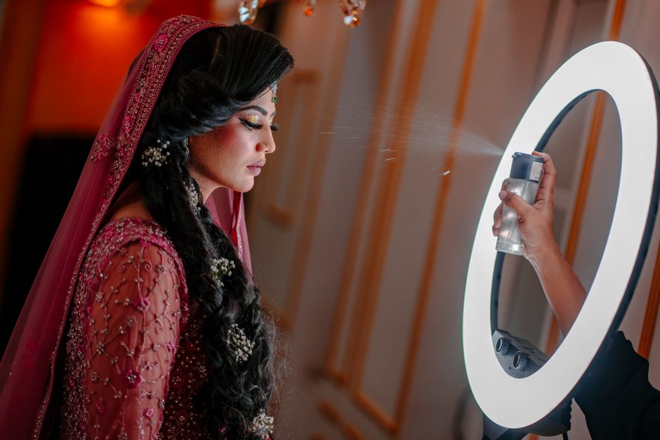 A stunning bride in traditional attire having makeup set under a ring light.