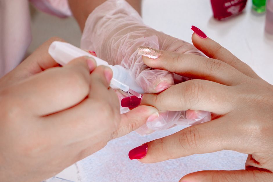 Close-up of a nail technician applying red nail polish during a professional manicure session.