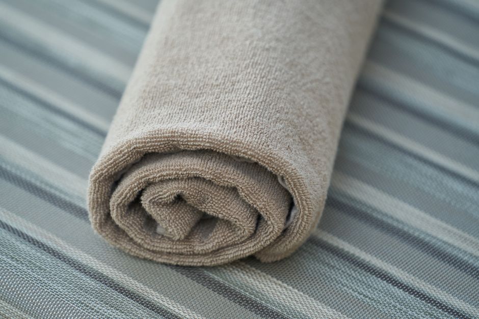 Close-up of a soft beige cotton towel rolled neatly on a striped fabric surface. Perfect for home decor or textile themes.