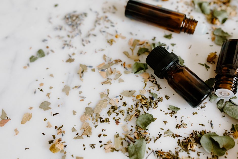 Aromatherapy setup with essential oil bottles and dried herbs on a white surface for holistic healing.