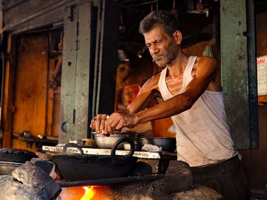 An elderly man cooks on a traditional stove in a bustling street market.