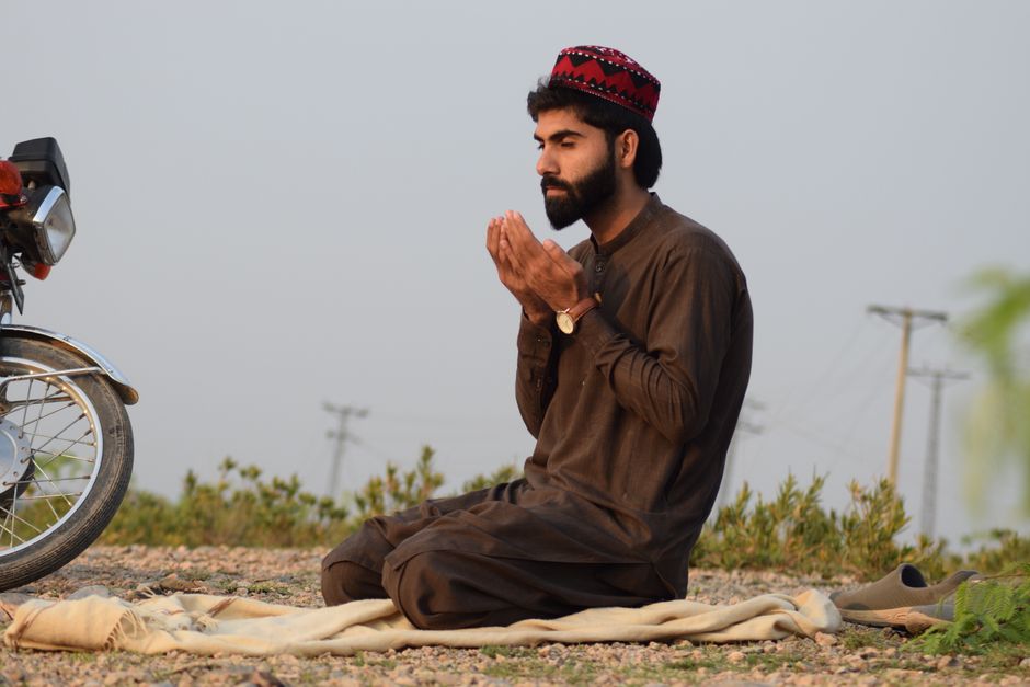 A man in traditional attire prays outdoors in Peshawar, Pakistan, showcasing cultural and spiritual themes.