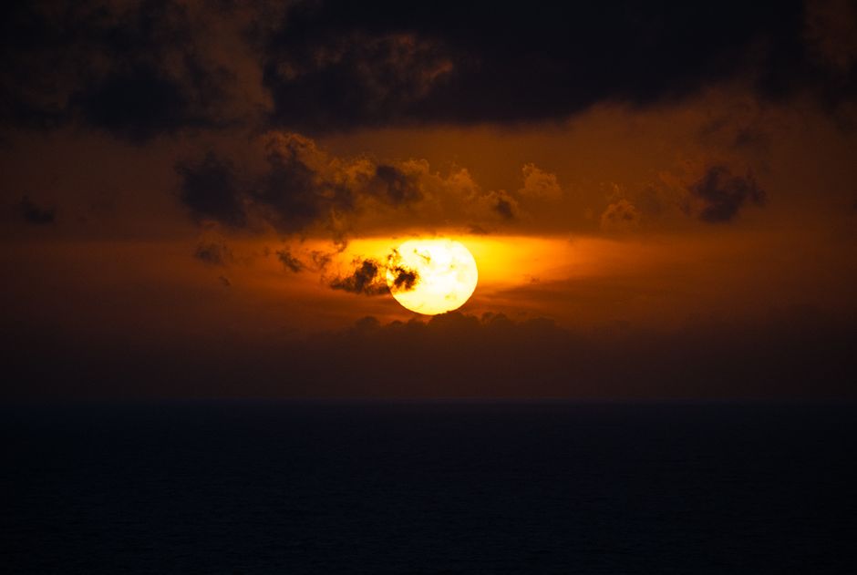 A breathtaking view of a fiery sunset over the ocean, casting a warm glow and dramatic clouds.