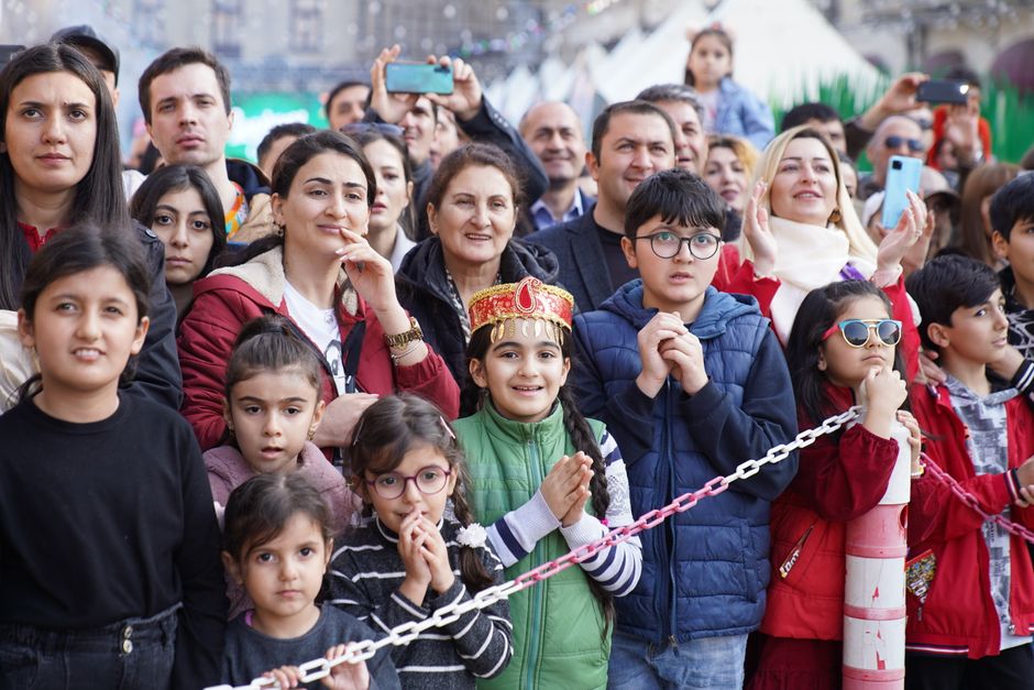 A diverse group of adults and children enjoy an outdoor festival, capturing joyful expressions.