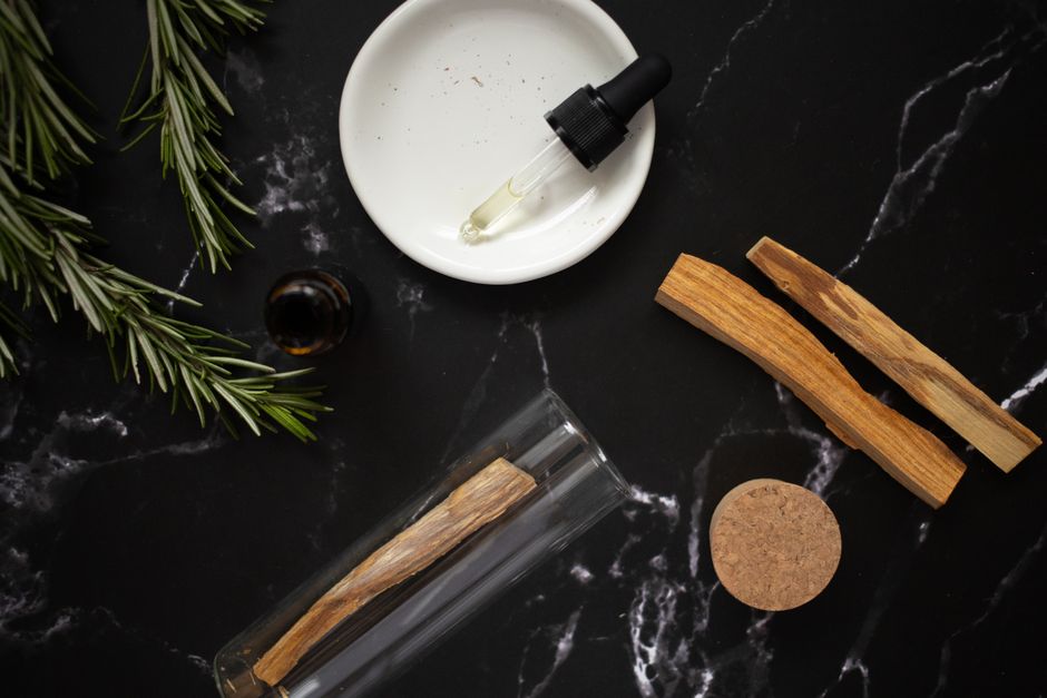 Top view of wooden sticks placed near plate with aromatic oil in pipette and fresh green branches of rosemary
