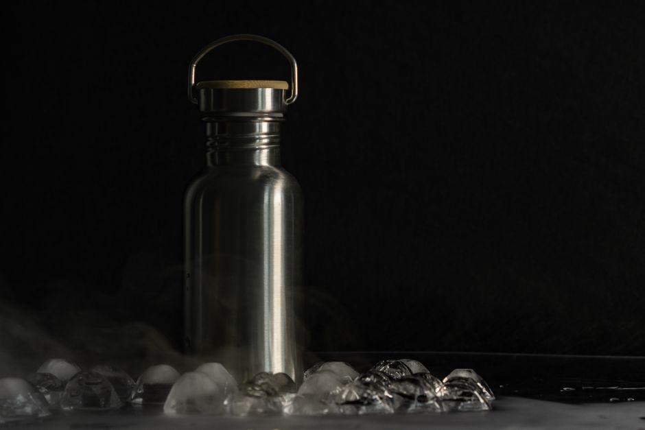 A stainless steel flask surrounded by ice cubes on a dark surface, offering a minimalist and sleek aesthetic.