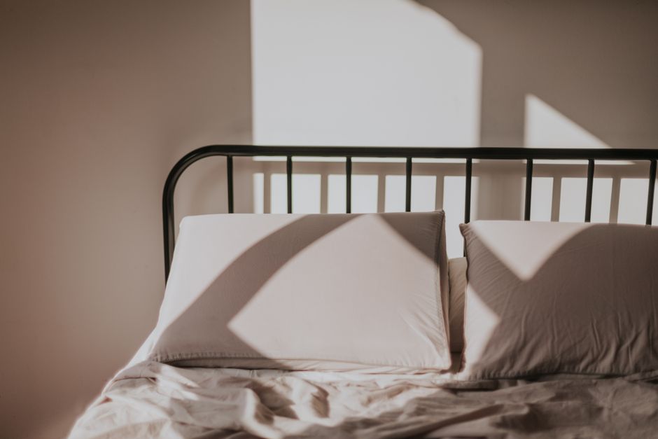 Sunlight casting geometric shadows on a bed with pillows, creating a serene morning atmosphere.