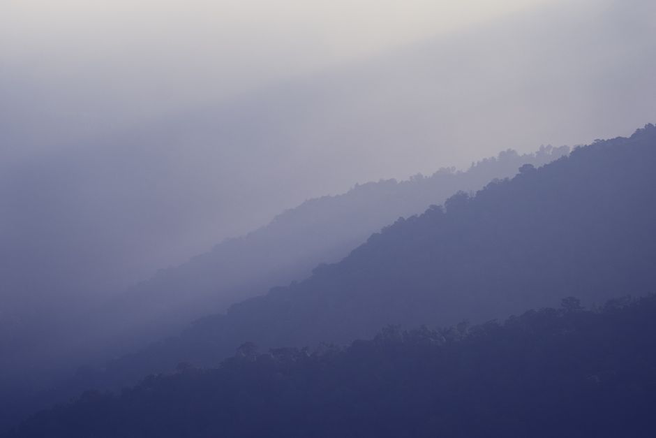 Serene blue mountain ridges under a foggy sky create a calming landscape.