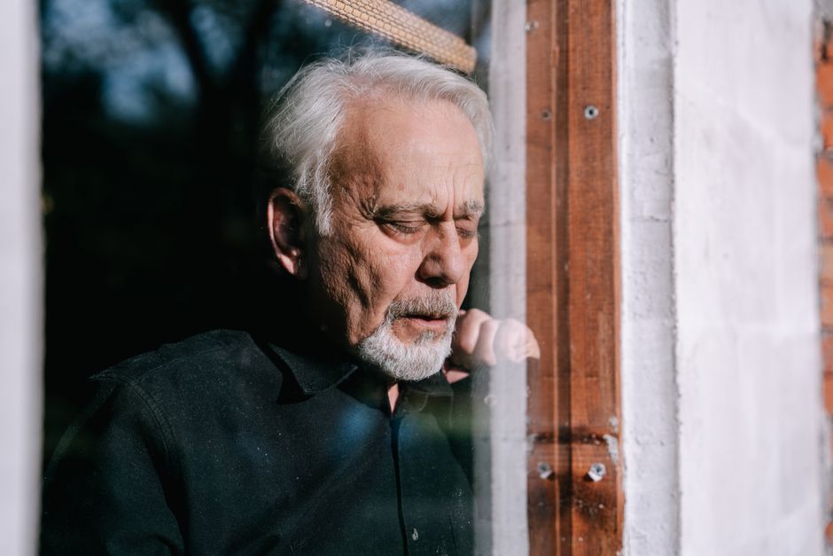 Portrait of a senior man with eyes closed, reflecting by a sunlit window indoors.