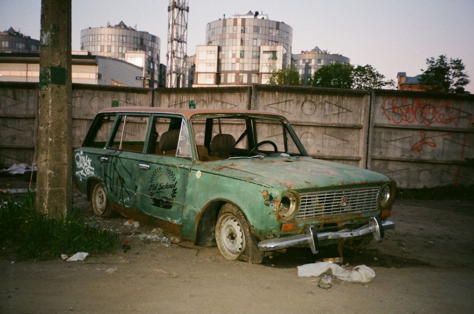 Abandoned vintage car in urban area with graffiti and rust.