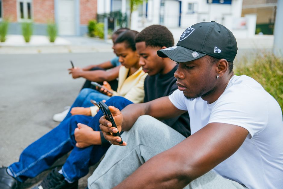 Group of young adults using smartphones seated outdoors in Brussels, capturing modern tech engagement.