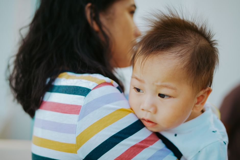 A woman lovingly holds an Asian baby boy indoors, showcasing a tender family moment.