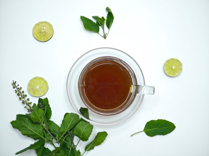 A cup of aromatic tulsi tea surrounded by fresh lime slices and basil leaves, offering a refreshing herbal beverage.