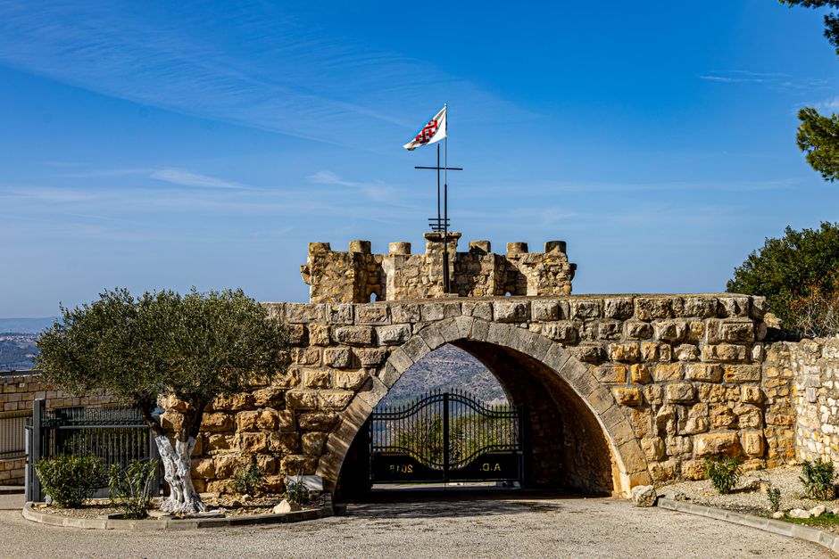 A historic stone archway featuring a flag atop a scenic landscape under a clear blue sky.