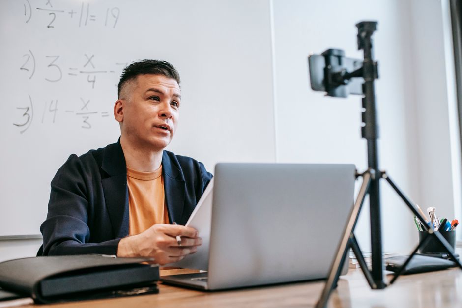 Male instructor conducting an online education session with a laptop and camera.