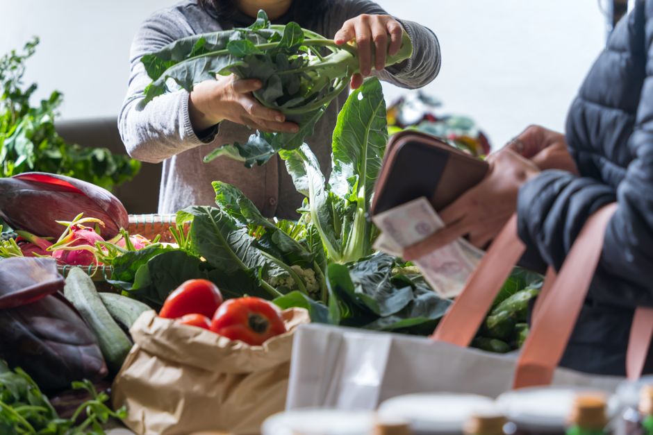 Hands exchanging fresh vegetables at a bustling farmers market stand.