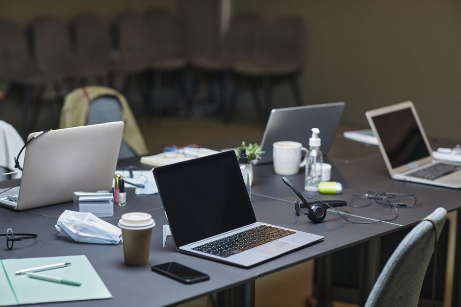 A cluttered office desk setup featuring multiple laptops, coffee cup, and office supplies for a busy workday.