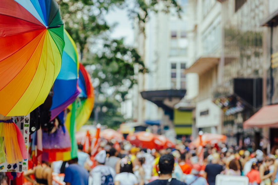 Colorful rainbow umbrellas adorn a lively outdoor city festival with a bustling crowd.