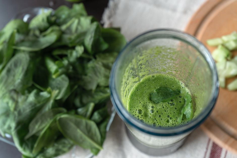 A refreshing green smoothie made with fresh spinach and cucumber on a wooden board.