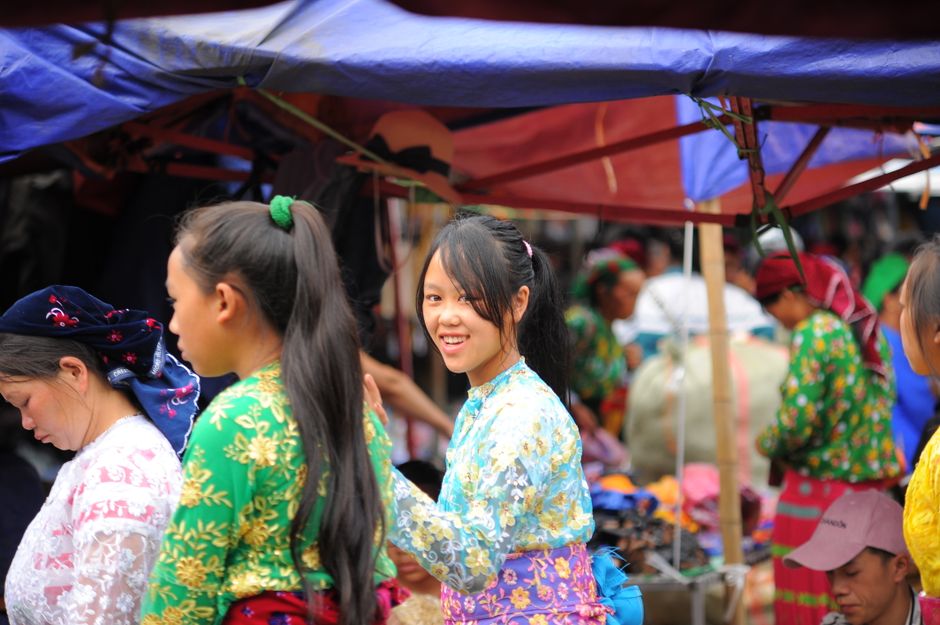 A bustling outdoor market scene with women in colorful traditional outfits, capturing a moment of cultural exchange.