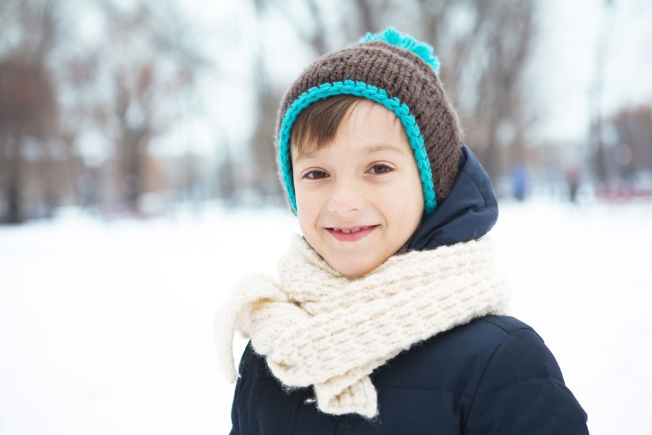 Cheerful child in knitted hat and scarf enjoying a snowy winter day outdoors.