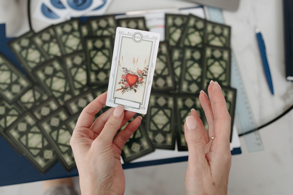 Hands holding a tarot card with heart design, surrounded by scattered cards emphasizing mystery.