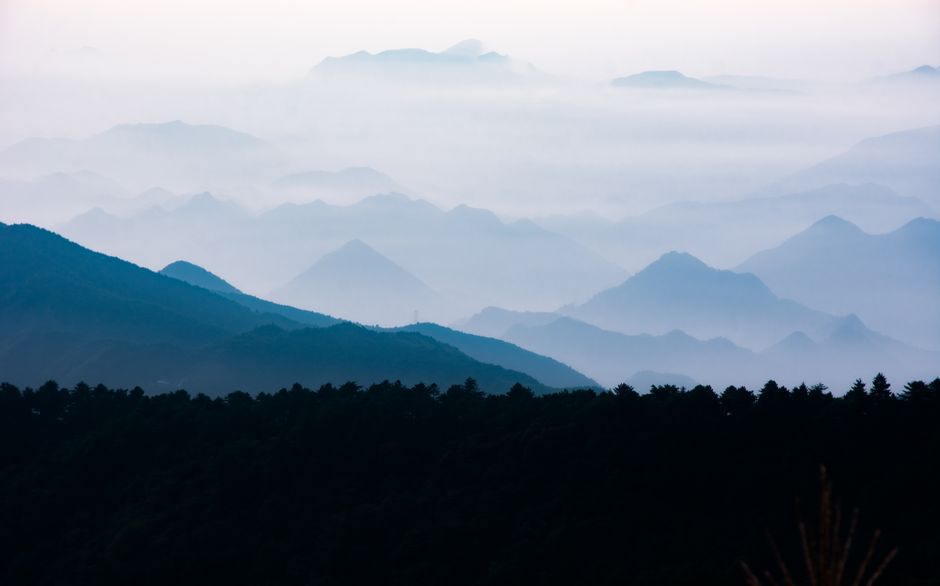 A serene view of layered mountains enveloped in mist, creating a mystical atmosphere.
