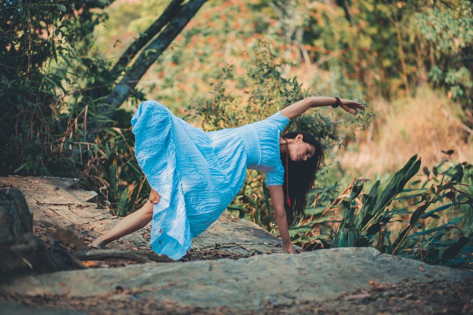 Full body of barefoot female in dress doing lateral bend supported by leg and arm in nature during yoga session