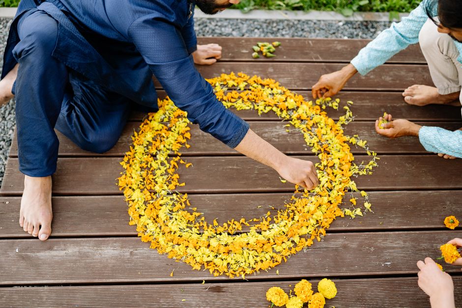 People arranging vibrant yellow petals into a circular floral design on wooden floor.