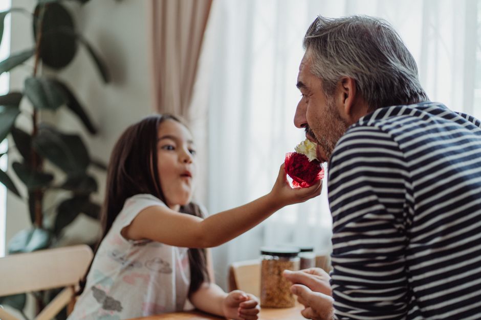 A joyful father and daughter enjoying a dessert at a dining table, sharing a sweet moment.