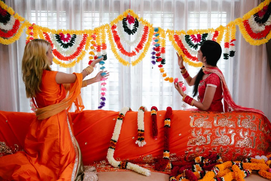 Two women in traditional attire decorating a room with colorful floral garlands.