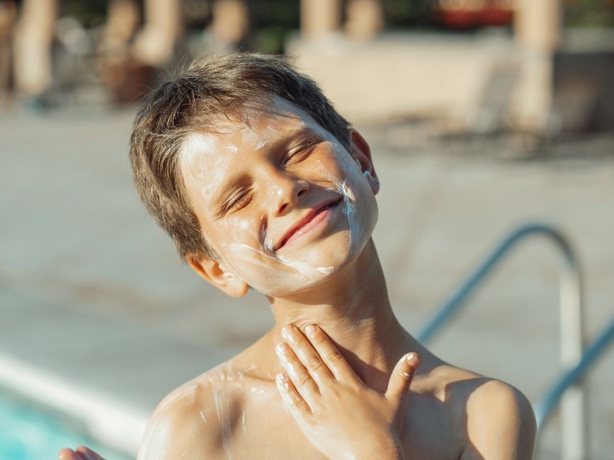 Smiling boy applying sunscreen, enjoying sunny day by the pool.