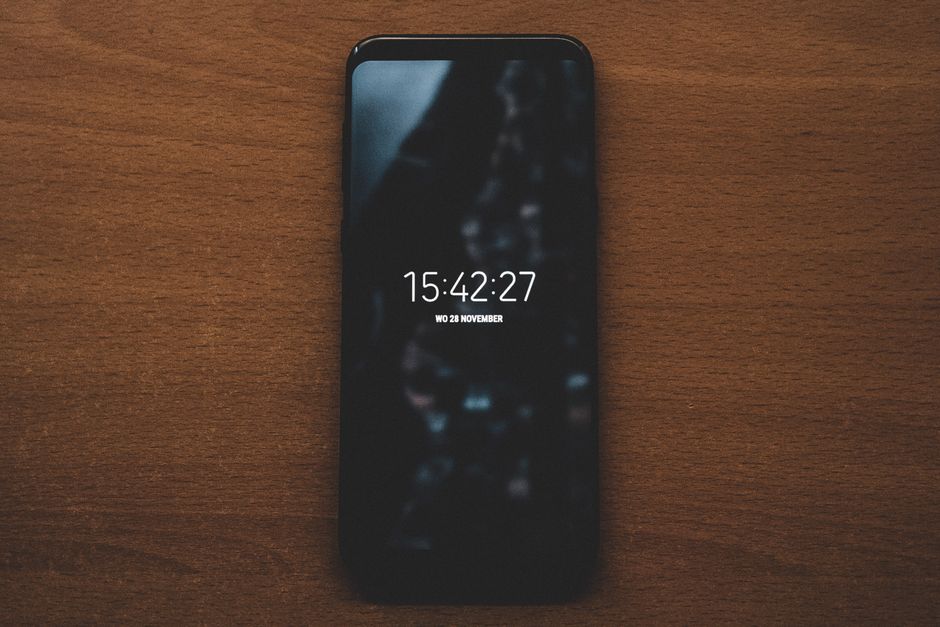 A smartphone displaying time sits on a wooden surface, showcasing modern technology.