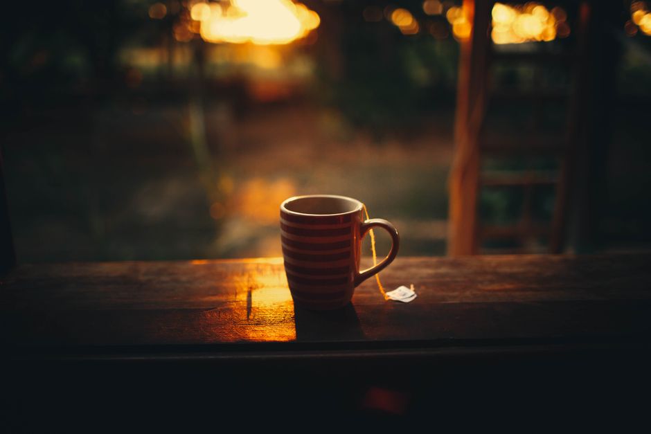 From above of cup of hot tea placed on balcony wooden railing against blurred green forest during bright sunrise