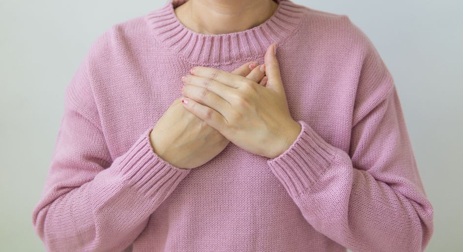 Unrecognizable female wearing pink sweater standing on white background with crossed hands on chest in light room in daytime inside
