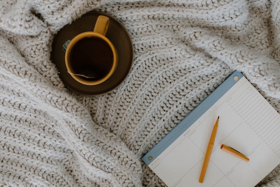 A relaxing flat lay of tea, planner, and warm knitted blanket for planning days.