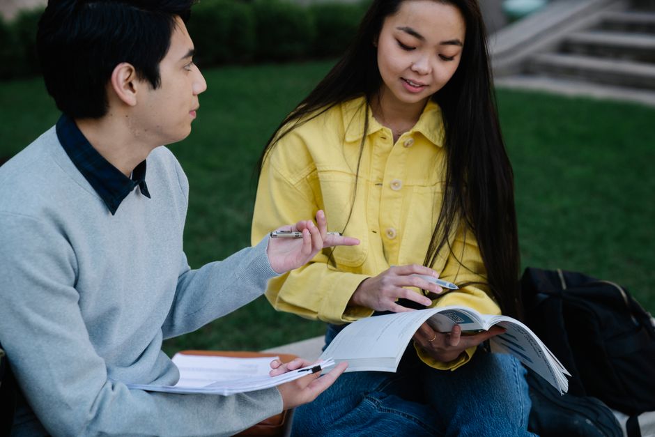 Two students engage in outdoor study session with textbooks and notes.