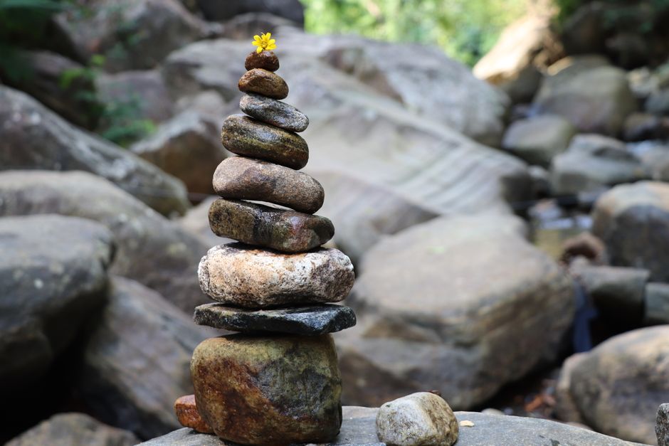 A tranquil stone stack with a yellow flower on top amidst a natural rocky setting.