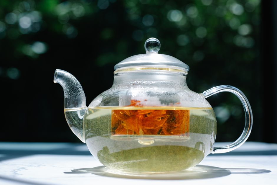 A clear glass teapot with herbal tea, captured in bright sunlight, showcasing the infusion process.
